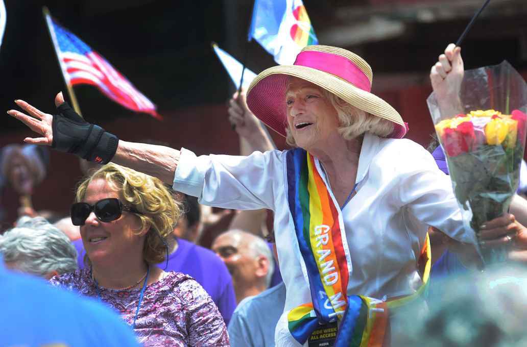Edie Windsor, aged 84, wearing a rainbow sash surrounded by crowds and Pride flags